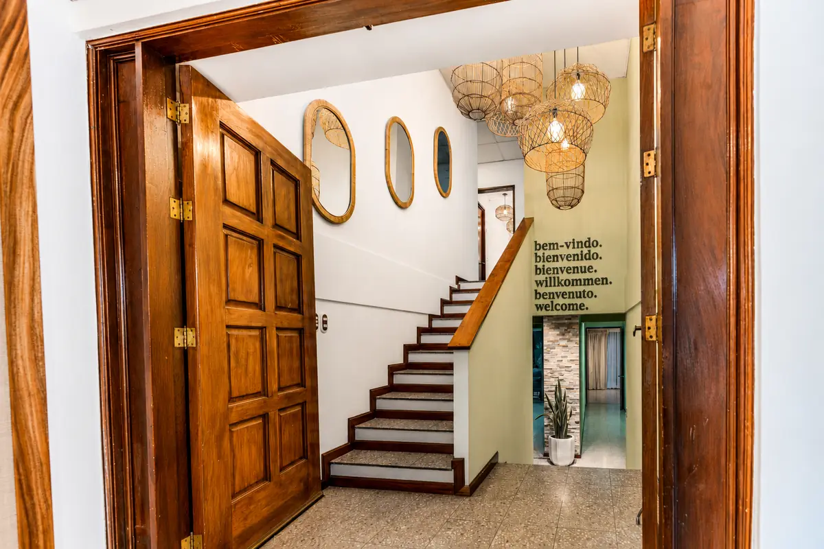 Entrada y escalera de Casa Lúmina con lámparas de ratán y la palabra bienvenido en varios idiomas